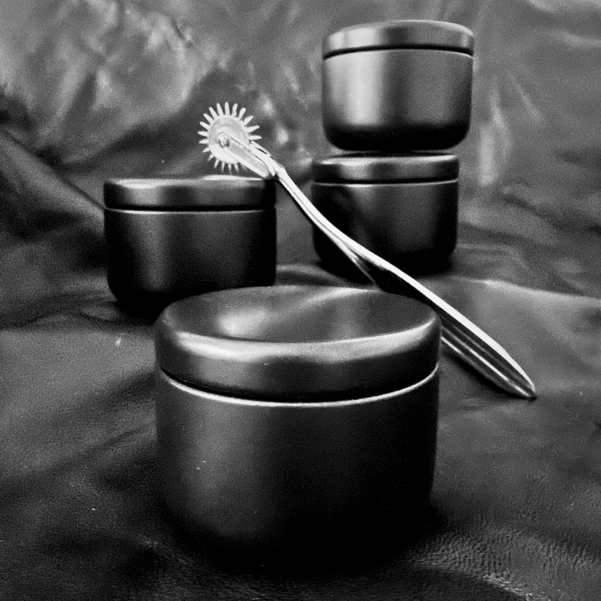 Kinkette Discovery Set — four black matte travel candle tins with Wartenberg wheel on dark leather surface