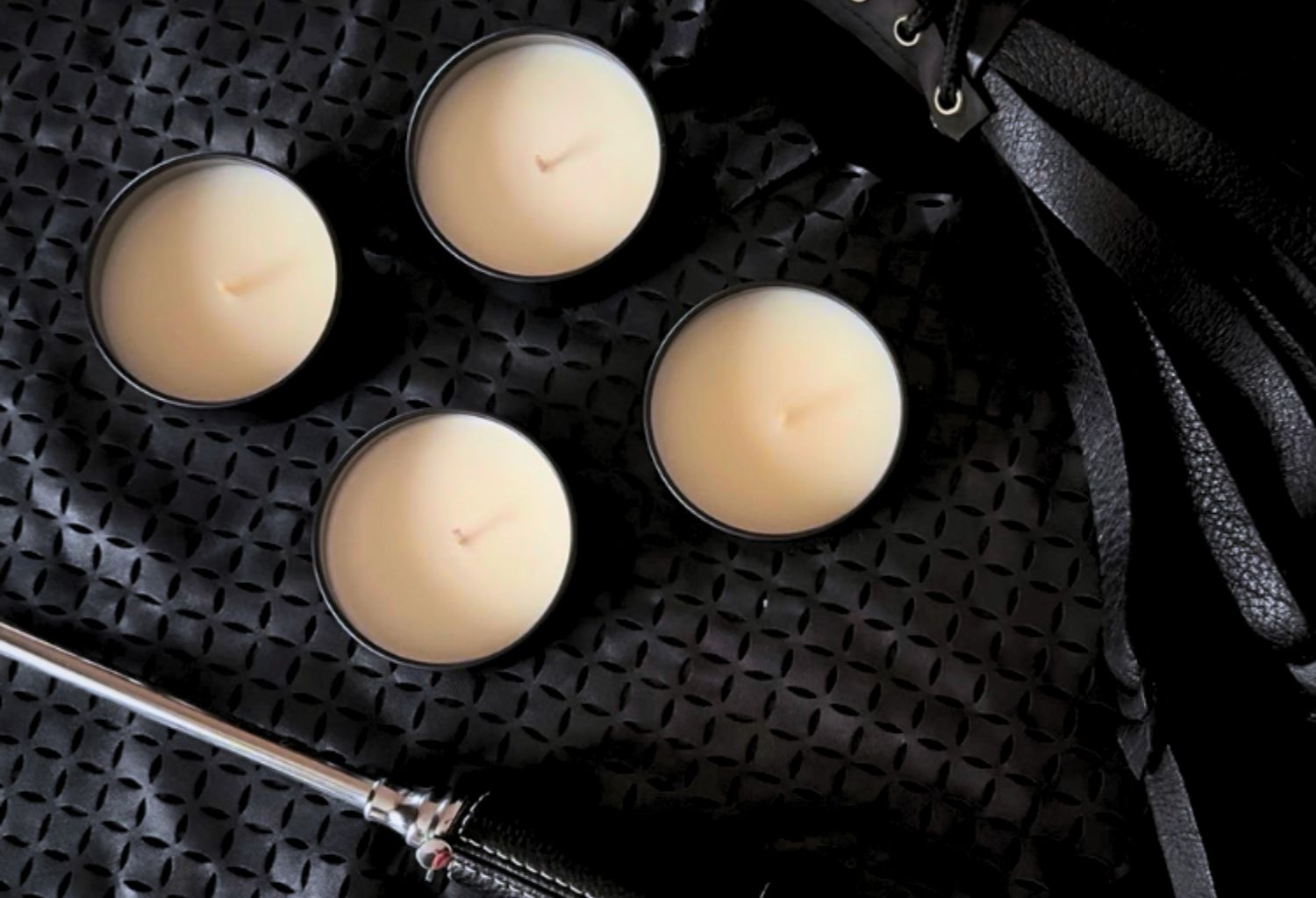 Four candles against a black background with a leather flogger and a lighter