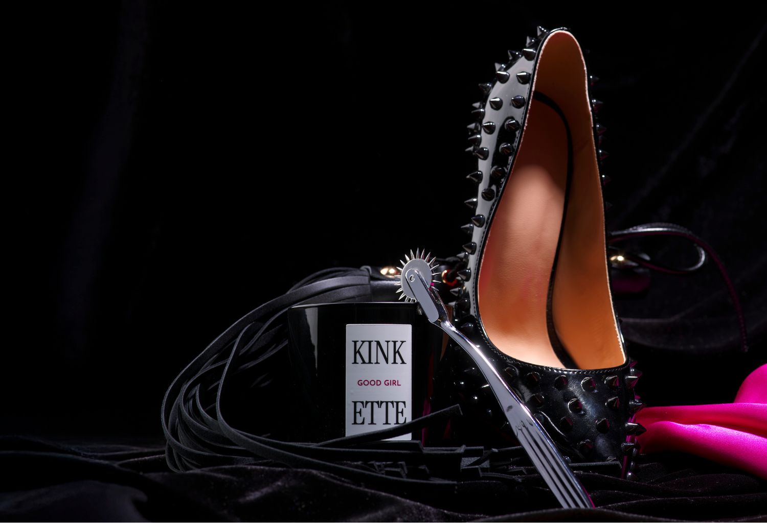Black candle, spiky shoe, and leather flogger against a black background