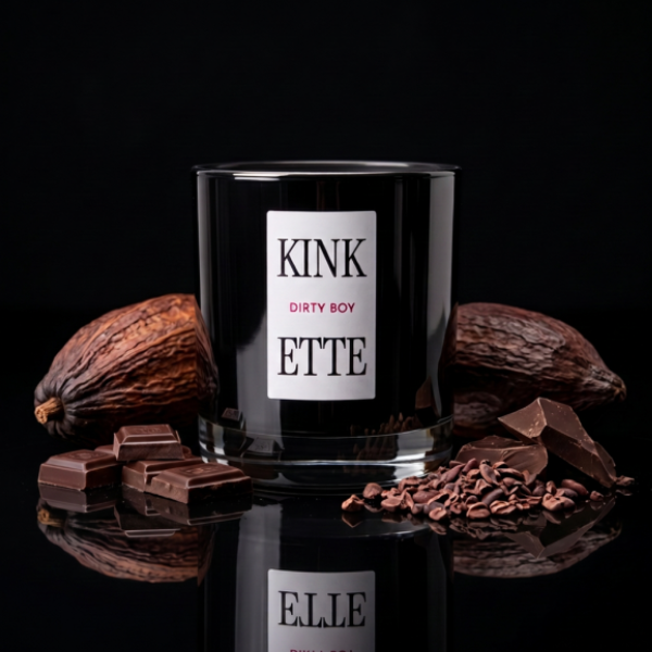 Candle with 'KINKETTE DIRTY BOY' label surrounded by cocoa beans and chocolate pieces on a black background