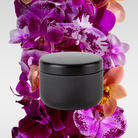 Kinkette discovery travel candle black tin surrounded by purple and orange orchids — 3 oz paraffin-free luxury candle
