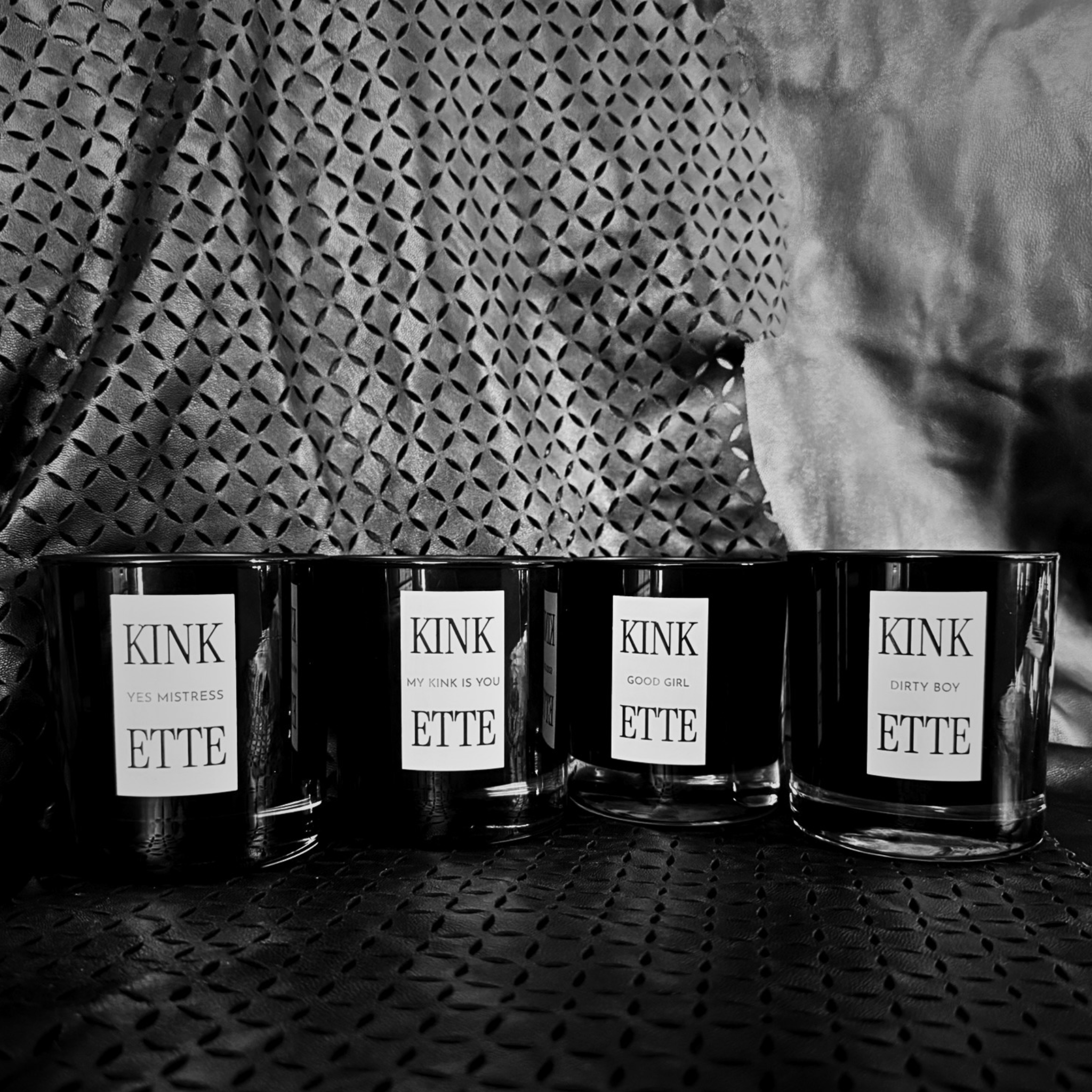 All four Kinkette Signature Candles — YES MISTRESS, MY KINK IS YOU, GOOD GIRL, DIRTY BOY — on embossed leather
