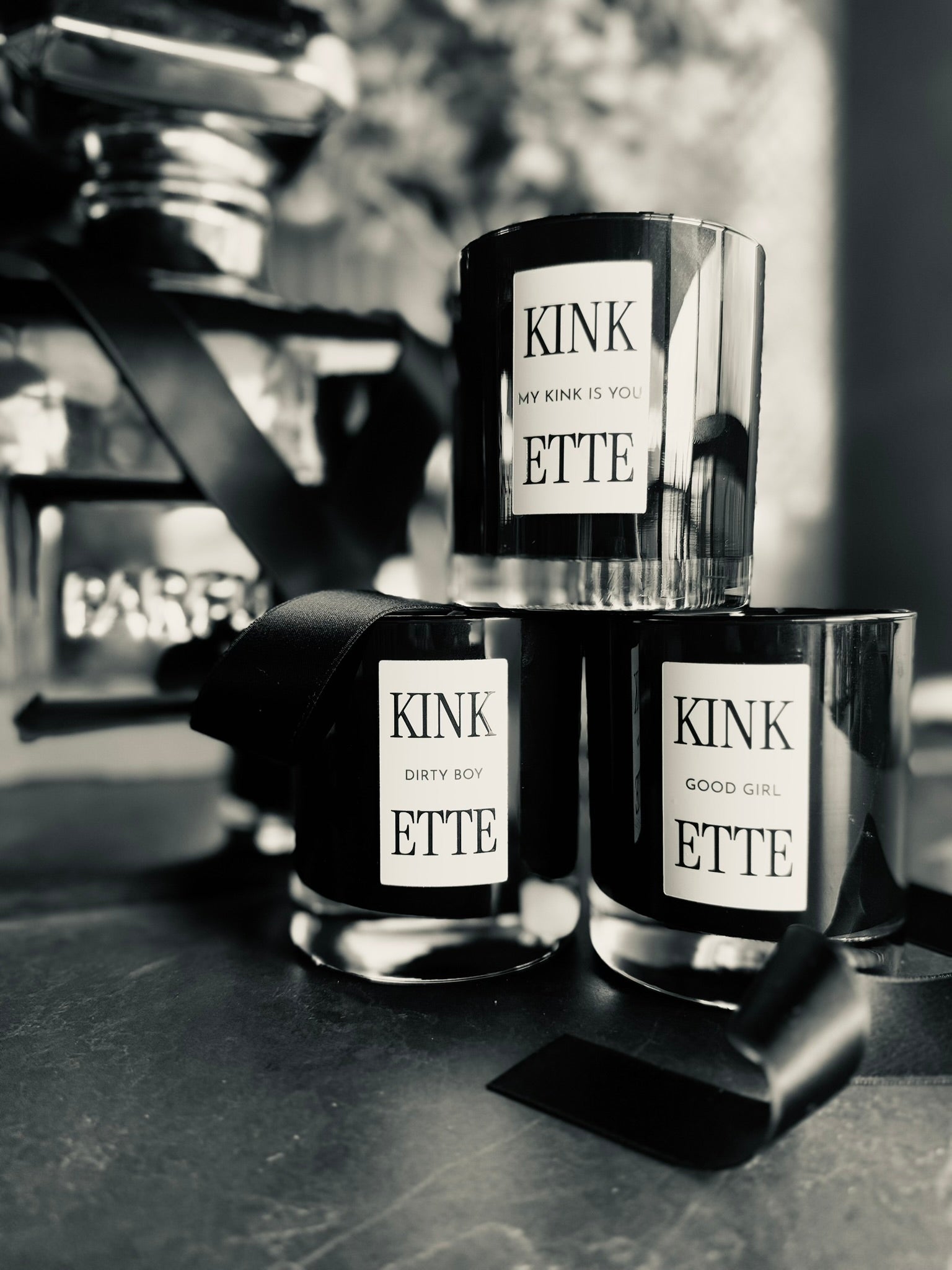 Three Kinkette Signature Candles — MY KINK IS YOU, DIRTY BOY, GOOD GIRL — styled in black and white editorial with perfume bottle in background